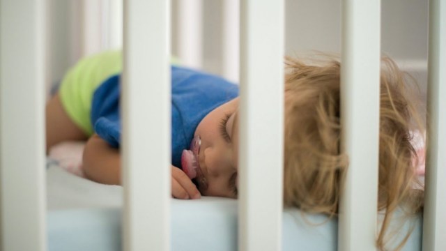 a baby with a pacifier sleeps in his crib
