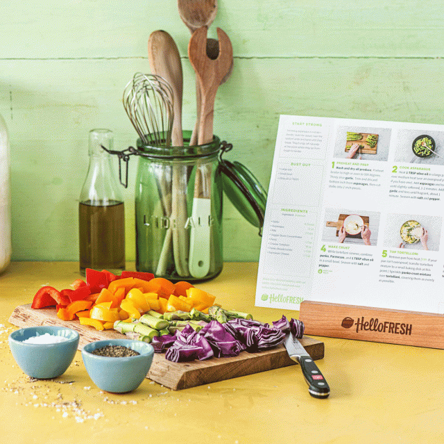 Carrots, bell peppers and other chopped vegetables are on a cutting board with utensils next to a recipe from the meal delivery service HelloFresh