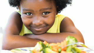 A young girl who is usually a picky eater sits smiling behind a healthy meal at the dinner table