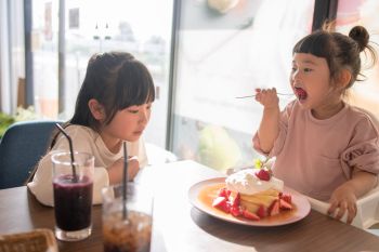 two kids eat free at a restaurant serving waffle with strawberries and whipped cream while their mom is equipped with a bag full of things to do with toddlers in restaurants