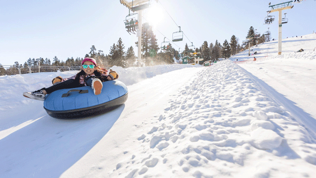 A little girl wearing goggles slides down a hill on an inner tube at a snow play area near LA