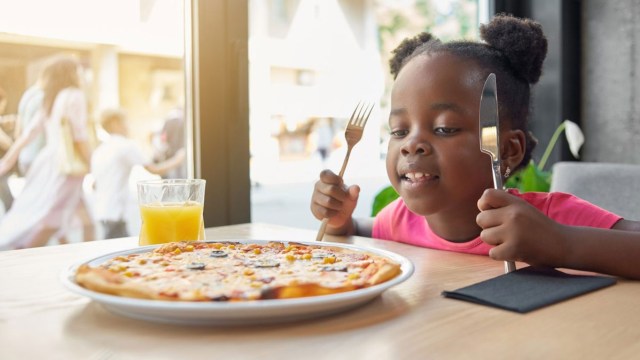a girl eats pizza with a fork and knife in hand
