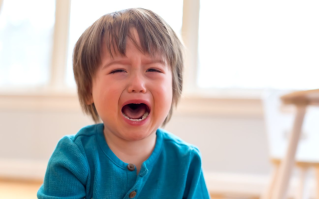 a boy wearing a blue shirt is crying on the floor during a toddler tantrum