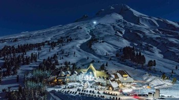 a snowy mountain with a village lit up against the night sky is an easy winter getaway near Portland timberline lodge