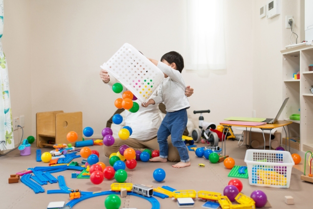 a boy dumps colorful balls from a white laundry basket during indoor play on a rainy day