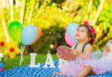 baby girl at a first birthday party outdoors holding a lollipop