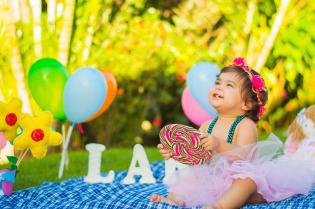 baby girl at a first birthday party outdoors holding a lollipop