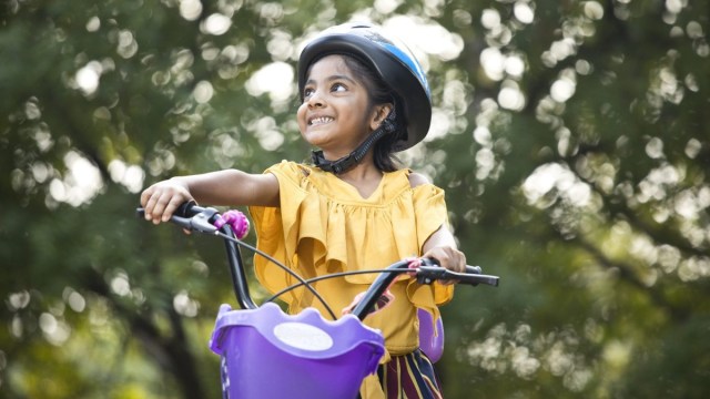 a young girl with a purple helmet smiles on a bike ride, things to do with kids