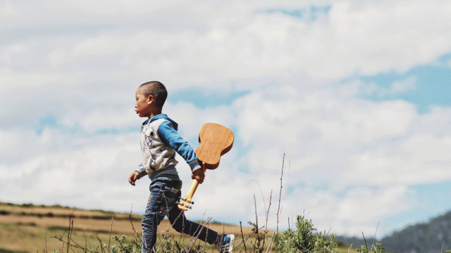 A boy walks through a field holding a guitar on the way to play a musical game