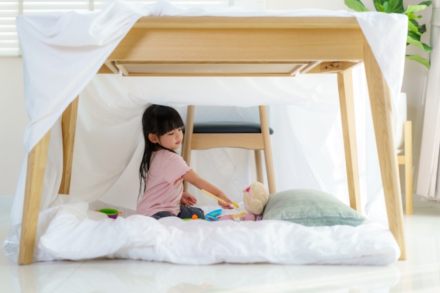 a young girl plays with an indoor fort, a rainy day activities, with a sheet over a bed