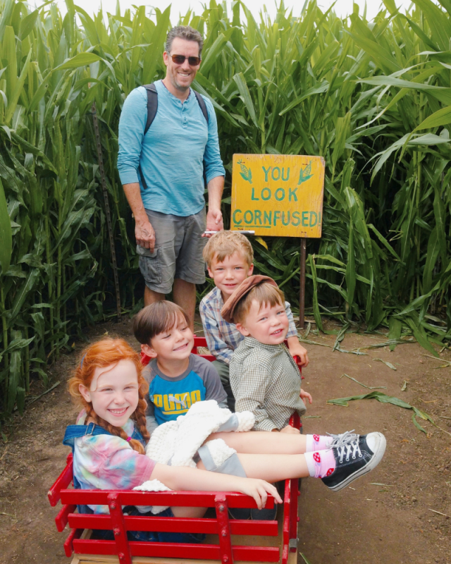 Four kids in a wagon and dad is pulling them through the corn maze. Sign says, "You look corn-fused."
