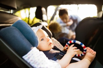 white baby girl in car seat with siblings behind her
