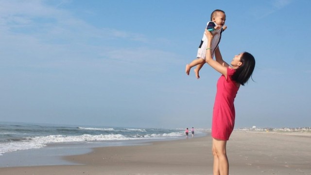 엄마가 해변에서 아기를 머리 위로 안고 있다