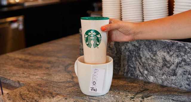 A hand holding a reusable Starbucks cup at a Starbucks counter.