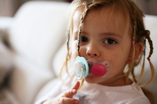 toddler girl with two pacifiers in her mouth - should you reuse baby gear