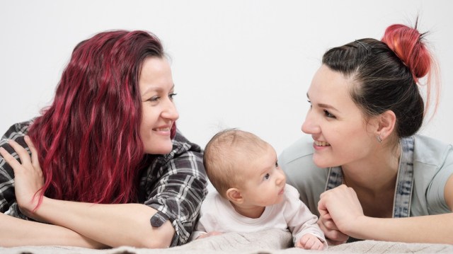 Two moms smile at each other while a baby lies between them