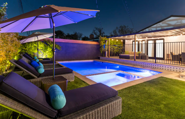 Pool lit up at night with purple lights and patio furniture surrounding it.