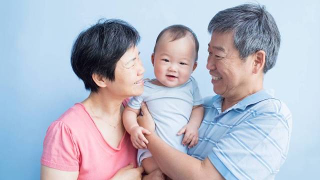 Two asian grandparents hold and smile at their grandchild between them