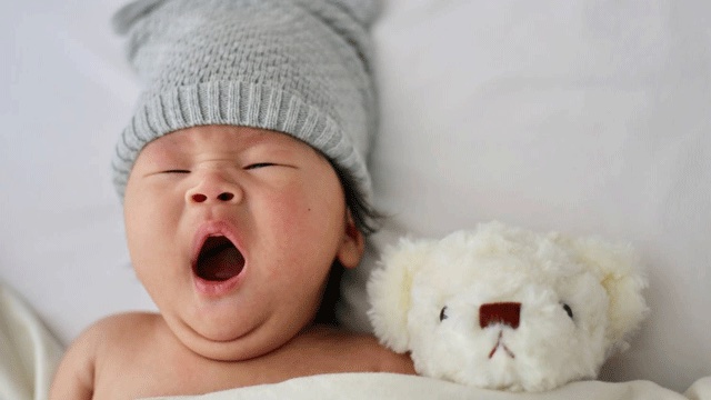 a yawning baby with a stuffed teddy bear