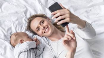 mom & baby taking selfie laying on white bed - baby hacks