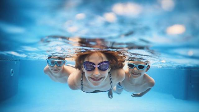three kids swim underwater at an indoor swimming pool