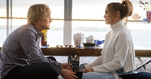 Owen Wilson and jennifer lopez sit on the floor facing each other in front of table