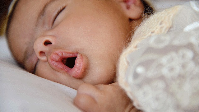 a newborn sleeps with its mouth open and hands close to its face, newbon sleep tips