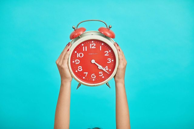 hands holding red old-fashioned alarm clock with blue background - baby hacks