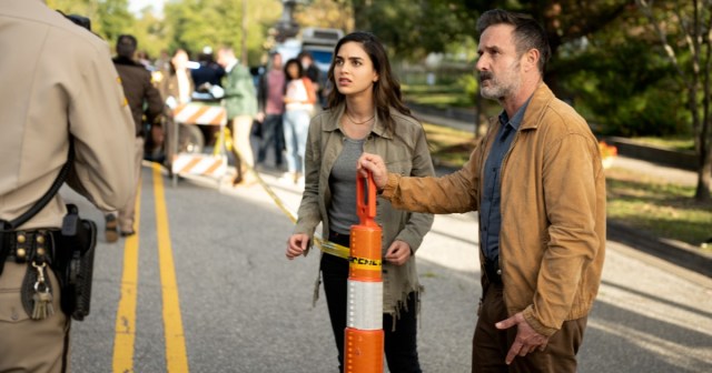 Melissa Barrera and David Arquette stand in a road talking to a police officer