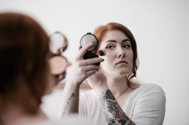 woman with tattoo and red hair putting on makeup - new mom beauty tips