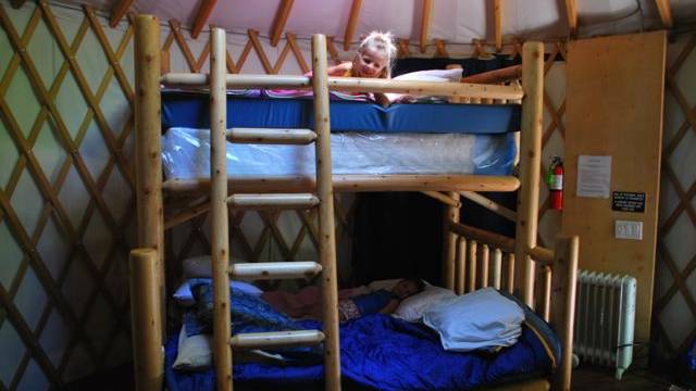 a girl peeks over the bunk of her bed in a yurt camping