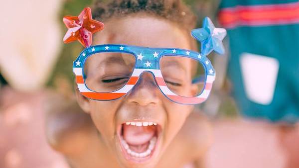a happy kid wears red white and blue sunglasses on 4th of july