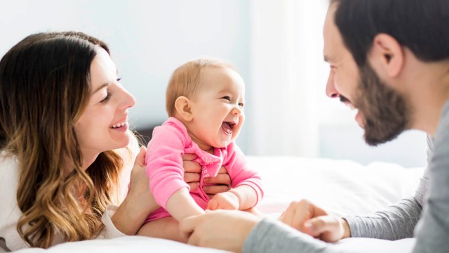 A baby laughing on the bed with mom and dad.