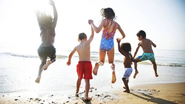 kids hold hands and jump in the water at the beach, family activities this month