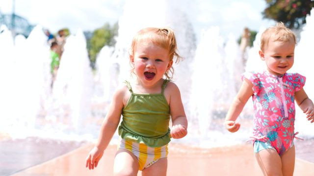 two toddlers playing at a splashpad in swimsuits in summer