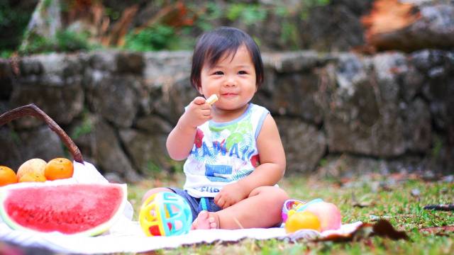 a baby sits on a picnic blanket during a family activity this month