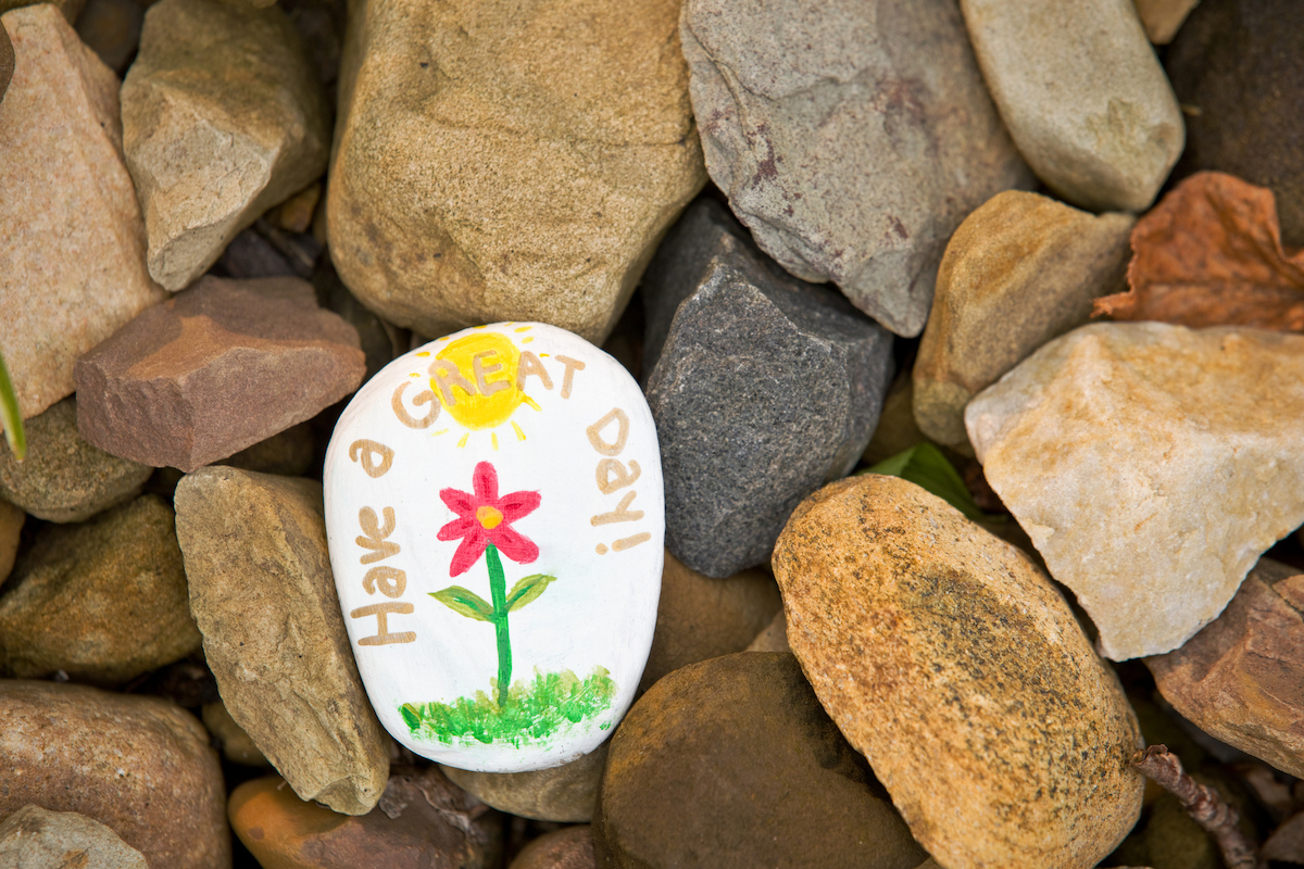 painted rock saying have a great day with a flower 