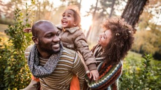 a family of three hikes through a sunny forest in fall