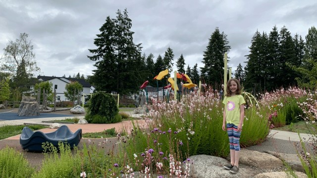 a girl stands by a playground on bainbridge island, an easy weekend trip from seattle with a ferry ride