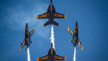 four blue angel show pilots fly in formation with blue sky background