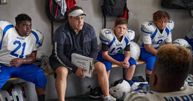Kevin James speaks to young football players in a locker room