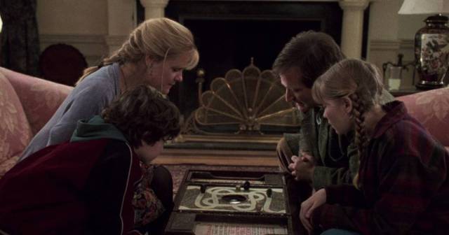 A man, woman, boy, and girl bend down over a board game in Jumanji