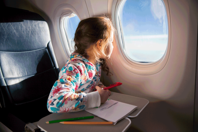 young child looking out window of airplane on family vacation