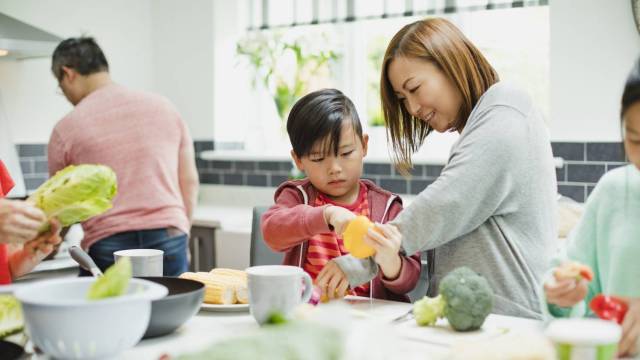 A mother and son chop vegetables together on a kitchen island