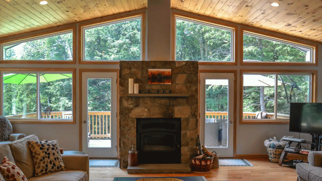 a cozy cabin includes a stone fireplace and floor to ceiling windows where you can see the forest