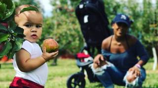 a toddler holds a u pick apple in its hand while mom looks on from the background