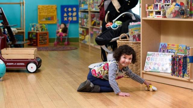 A little girl plays on the floor with a car at a consignment shop