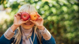 child holding up two apples in front of her face at apple orchard