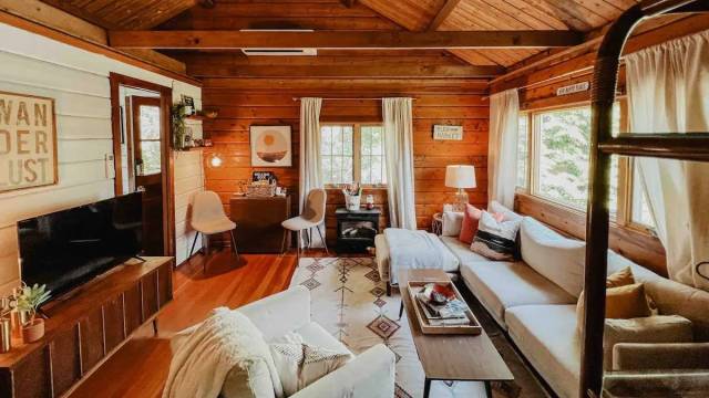 the interior of a cozy log cabin with color coordinated neutral furniture and sunshine in the windows