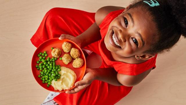 a girl smiles with a plate of food in her hand from yumble, meal delivery service